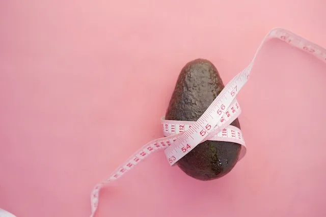 Avocado wrapped in a measuring tape on a pink background