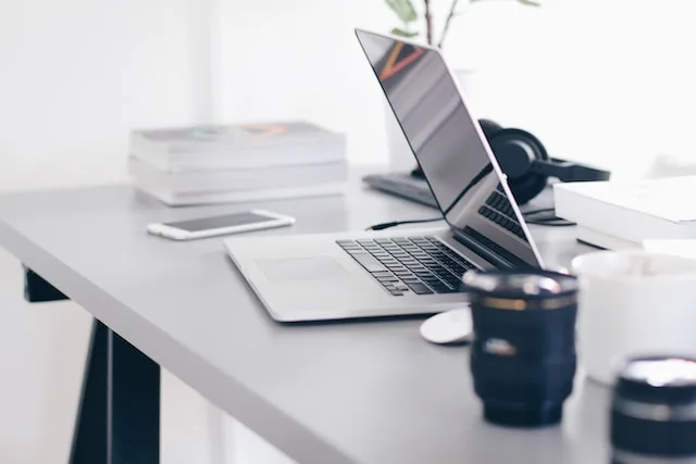 Laptop and notebooks on a desk with headphones and a camera lens